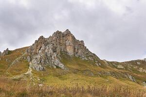 lindo rochoso penhasco em uma montanha cume dentro a distância e a outono alpino Prado dentro a primeiro plano foto