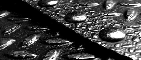 ai gerado macro tiro do brilhante água gotas em uma texturizado Preto perfurado metal superfície foto