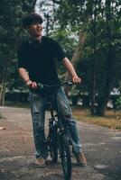 jovem bonito barbudo homem levando uma pausa enquanto viajando a cidade com dele bicicleta usando dele digital tábua olhando longe pensativamente foto