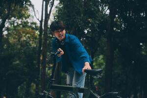 jovem bonito barbudo homem levando uma pausa enquanto viajando a cidade com dele bicicleta usando dele digital tábua olhando longe pensativamente foto