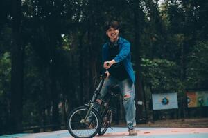 jovem bonito barbudo homem levando uma pausa enquanto viajando a cidade com dele bicicleta usando dele digital tábua olhando longe pensativamente foto