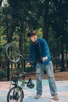 jovem bonito barbudo homem levando uma pausa enquanto viajando a cidade com dele bicicleta usando dele digital tábua olhando longe pensativamente foto