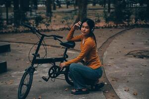 feliz jovem ásia mulher enquanto equitação uma bicicleta dentro uma cidade parque. ela sorriu usando a bicicleta do transporte. ambientalmente amigáveis conceito. foto