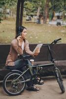 feliz jovem ásia mulher enquanto equitação uma bicicleta dentro uma cidade parque. ela sorriu usando a bicicleta do transporte. ambientalmente amigáveis conceito. foto