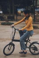 feliz jovem ásia mulher enquanto equitação uma bicicleta dentro uma cidade parque. ela sorriu usando a bicicleta do transporte. ambientalmente amigáveis conceito. foto