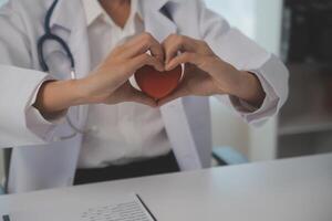 mãos do médico mulher segurando vermelho coração, mostrando símbolo do amor, humano Apoio, suporte para paciente, promovendo médico seguro, cedo checar para assistência médica, cardiologista ajuda. fechar acima do objeto foto