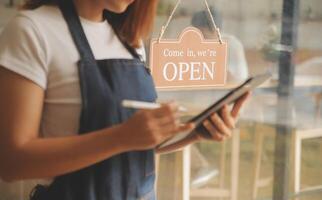 startup bem sucedido pequeno empresário sme beleza garota stand com smartphone tablet no restaurante café. retrato do proprietário do café barista mulher bronzeada asiática. conceito de negócio de vendedor de sme empreendedor foto