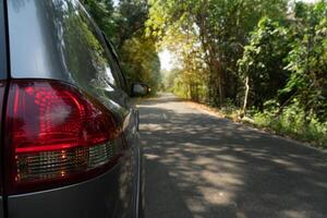 rabo luz do cinzento carro dirigindo em a asfalto estrada. floresta este cobre a em torno da área. foto