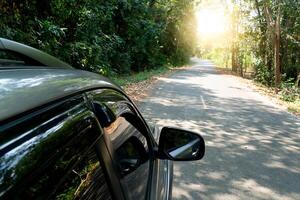 carro em a asfalto estrada dentro a floresta com Sol luz e lente flare. em ambos lados do a estrada lá estão verde florestas. foto