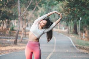 corrida conceito, em forma jovem mulher realizando uma lado esticam exercício em uma pacífico parque caminho cercado de árvores foto