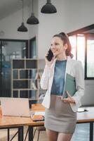 brilhante e moderno escritório configuração com uma alegre empresária segurando uma pasta e noivando dentro uma telefone conversação, incorporando ativo corporativo foto