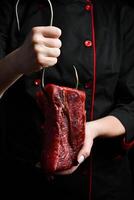 uma açougueiro detém uma peça do vitela em uma metal gancho. carne preparação. em uma Preto fundo. foto