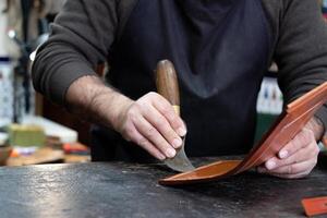 mãos do artesão trabalhando a couro com especial ferramenta dentro uma oficina foto