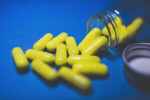 amarelo cor pílulas em azul fundo e transparente vidro farmacia garrafa. seletivo foco foto