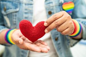 senhora asiática usando pulseiras de bandeira de arco-íris e segurar um coração vermelho, símbolo do mês do orgulho LGBT, comemorar anual em junho social de gays, lésbicas, bissexuais, transgêneros, direitos humanos. foto