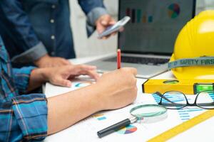 engenheiro asiático e equipe parceira aprendem e conversam com o projeto do plano da casa, gráfico e capacete amarelo e ferramentas de construção de engenharia no trabalho de mesa. foto