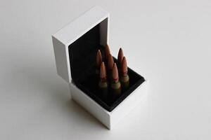 Sete balas dentro uma branco caixa com Preto aparar forrado acima gostar dentro uma revólver tambor em branco fundo foto
