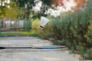 mão segurando uma badminton raquete para pegar uma queda branco peteca. conceito, jogando badminton ao ar livre, livre cair, gravidade, Esportes, lazer. foto