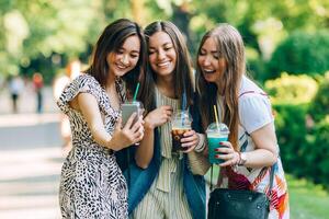 verão estilo de vida retrato multirracial mulheres apreciar agradável dia, segurando óculos do batidos. feliz amigos dentro a parque em uma ensolarado dia. melhor amigos meninas tendo diversão, alegria. estilo de vida. asiático, judia e foto