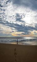 jovem homem em a de praia olhando às a pôr do sol, refletindo, espaço para texto foto