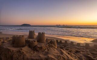 areia castelo em a de praia durante pôr do sol com espaço para texto foto