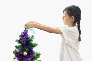 fofa criança apreciar decoração Natal árvore dentro a manhã dia branco luz fundo foto