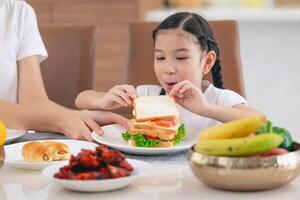 ásia fofa filha feliz apreciar comendo saudável Comida manhã refeição vegetal salada sanduíche foto