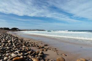 oceano de praia com ampla pedras e areia debaixo uma azul céu e nuvens foto