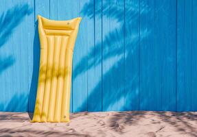 amarelo inflável colchão contra azul de madeira parede em de praia areia foto