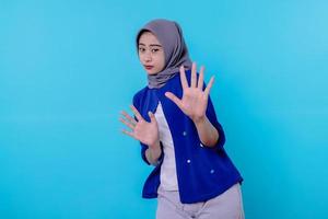 retrato de uma mulher usando um hijab mostrando um gesto de parada na parede azul foto