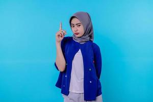jovem carismática bonita com hijab apontando isolado em fundo azul claro foto