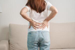 mulher tendo costas corpo dor durante sentado em sofá às lar. adulto fêmea com músculo dor vencimento para piriforme síndrome, baixo costas dor e espinhal compressão. escritório síndrome e médico conceito foto