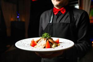 homem dentro Preto camisa e vermelho arco gravata segurando uma prato do Comida foto