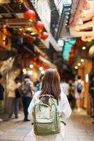 mulher viajante visitando dentro Taiwan, turista com chapéu e mochila passeios turísticos e compras dentro Jiufen velho rua mercado. ponto de referência e popular atrações perto Taipei cidade. viagem e período de férias conceito foto