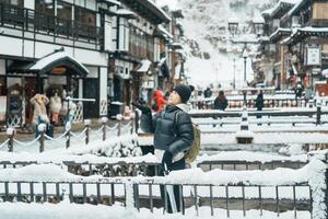 mulher turista visitando ginzan Onsen dentro Yamagata, feliz viajante passeios turísticos japonês Onsen Vila com neve dentro inverno temporada. ponto de referência e popular para atração dentro Japão. viagem e período de férias conceito foto