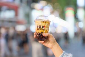 mulher mão segurando Castanho açúcar boba leite chá com tapioca pérolas, xing fu Espiga marca conhecido para fazer a melhor mão trabalhada Castanho açúcar boba. ximending noite mercado, Taipei, Taiwan, 02 abril 2023 foto