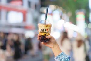 mulher mão segurando Castanho açúcar boba leite chá com tapioca pérolas, xing fu Espiga marca conhecido para fazer a melhor mão trabalhada Castanho açúcar boba. ximending noite mercado, Taipei, Taiwan, 02 abril 2023 foto