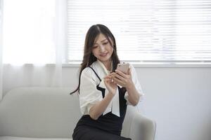 uma japonês mulher verificação Smartphone de controlo remoto trabalhos dentro a pequeno escritório foto