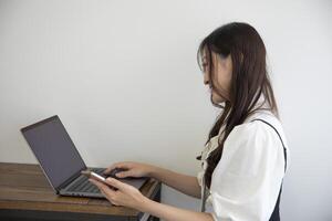 uma japonês mulher verificação Smartphone de controlo remoto trabalhos dentro a pequeno escritório foto