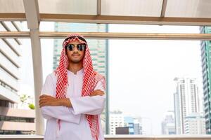 retrato do árabe homem de negocios em pé com braços cruzado borrado cidade fundo, muçulmano homem dentro oculos de sol em pé com braços cruzado foto
