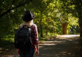 jovem caucasiano menina viaja dentro uma chapéu e com uma mochila através a floresta ou parque dentro a sombra do árvores .fundo borrado. Alto qualidade foto