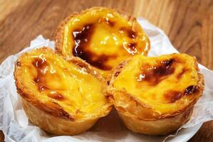 pastel de nata tortas ou Português ovo azedo em uma de madeira Castanho fundo. pastel de belém é uma pequeno torta com uma crocantes sopro pastelaria crosta e uma creme creme enchimento. doce sobremesa. foto