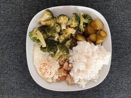 caseiro prato com brócolis, frito ovos com queijo, frango cozido carne, arroz e picles servido em branco prato foto
