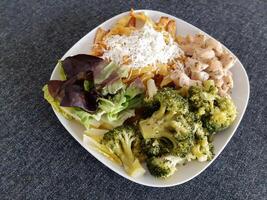 caseiro grelhado frango com francês fritas, brócolis, queijo e verde salada, servido em uma branco prato foto