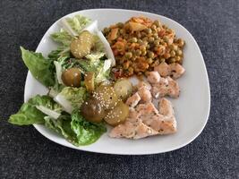 caseiro grelhado frango com verde salada, ervilhas ensopado e pepino picles servido em uma branco prato foto