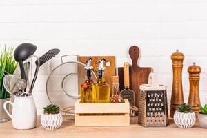 uma variedade do de madeira e metal cozinha utensílios em uma de madeira bancada. vidro garrafas com óleo dentro uma de madeira caso. à moda armazenamento área foto