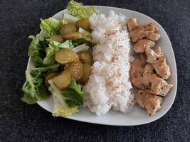 caseiro grelhado frango com verde salada, arroz Arroz a grega e pepino picles servido em uma branco prato foto
