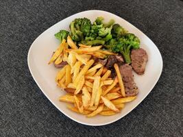 caseiro grelhado carne de porco com francês fritas e brócolis, servido em uma branco prato foto