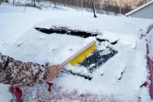 mão motorista usando escova varrendo neve em pára-brisas carro foto