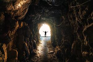 silhueta homem em pé em fim do natural caverna, subterrâneo túnel e luz brilha foto